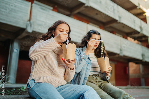 Women friends eating street food takeaway noodles
