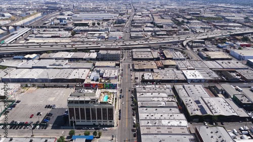 Urban landscape flying forward over industrial district with warehouses, rooftop pool, graffiti, highway interchange traffic in downtown Los Angeles, California