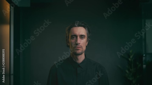 Close up portrait of young adult man with medium length hair in black button up shirt, neutral contemplative expression, indoor dark background, business lifestyle concept