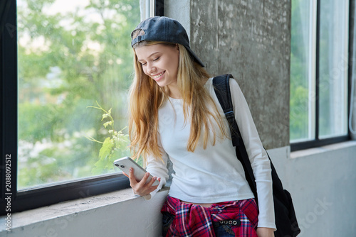 Smiling 16-year-old teenage girl using smartphone by the window