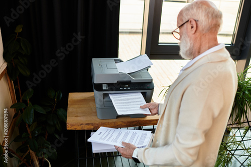 Canvas Print In a chic office, a senior businessman reviews printed documents, showcasing professionalism and elegance