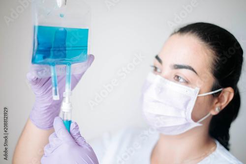 Close-up of a female nurse examining an intravenous fluid bag while preparing medical treatment in a professional clinical environment.