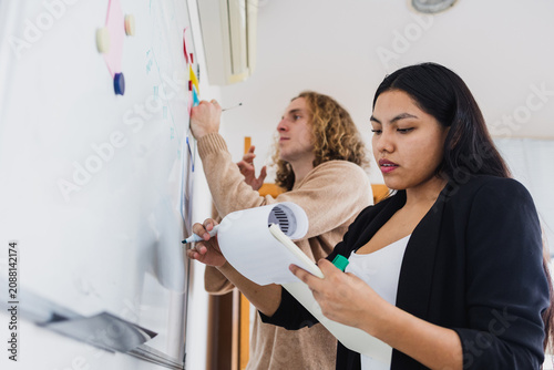 young latina Businesswoman writing on whiteboard in office in Latin America, Hispanic business people at workplace