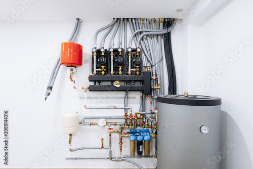 Indoor water heater manifold with insulated pipes pressure gauges and expansion tank in utility room