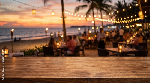 Wooden tabletop foreground with a blurred romantic beachside restaurant at sunset, featuring palm trees, string lights, and diners by the ocean.