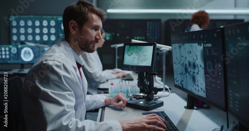 Scientist Uses Digital Microscope to Analyze Molecular Samples and Reviews MRI Brain Scans on Monitors in Hospital Laboratory While Female Researchers Develop Disease Treatments. Zoom out shot