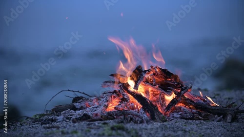 Bonfire burning on a rocky beach at dusk with sound of ocean waves