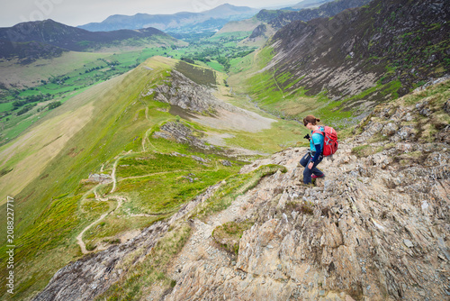 Принти на полотні A female hiker descending the rocky ridge of High Snab Bank, ridgeline, from the summit of Robinson with Newlands in the distance in the English Lake District, UK