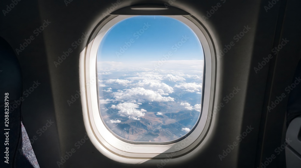 Fototapeta premium Airplane window view showing blue sky and fluffy white clouds above