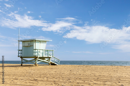 Empty sandy beach with lifeguard tower under blue sky