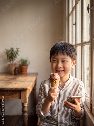 Asian boy holding ice cream and smartphone by the window