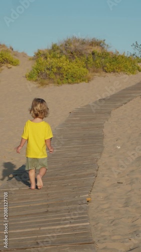 Toddler explores wooden path that winds through warm, golden dunes, fully embodying essence of summer adventures and pure innocence of childhood