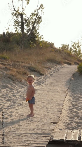 Small child walking along wooden planks set into sandy dune. A toddler's summer adventures and the pure innocence of childhood