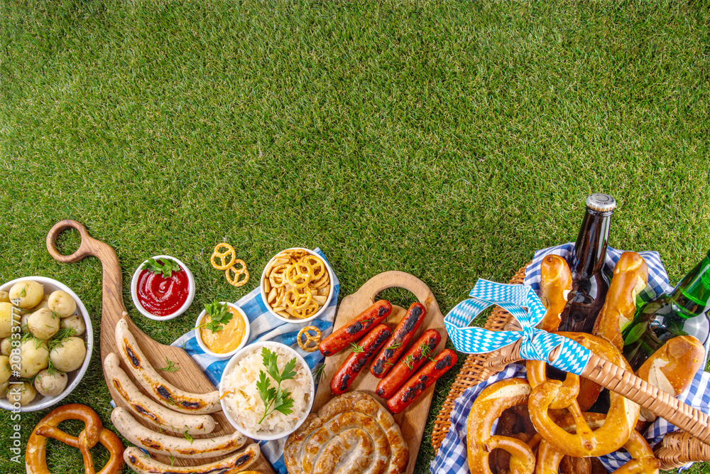 Fototapeta premium Oktoberfest picnic and barbecue food, bavarian party menu, bavarian sausages, pretzels, potato, sauerkraut, beer bottles, with picnic basket, checkered napkin tablecloth, Oktoberfest festive ribbon