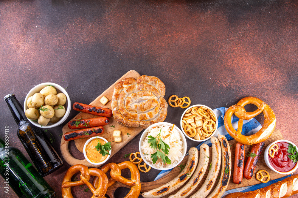 Fototapeta premium Oktoberfest picnic and barbecue food, bavarian party menu, bavarian sausages, pretzels, potato, sauerkraut, beer bottles, with picnic basket, checkered napkin tablecloth, Oktoberfest festive ribbon