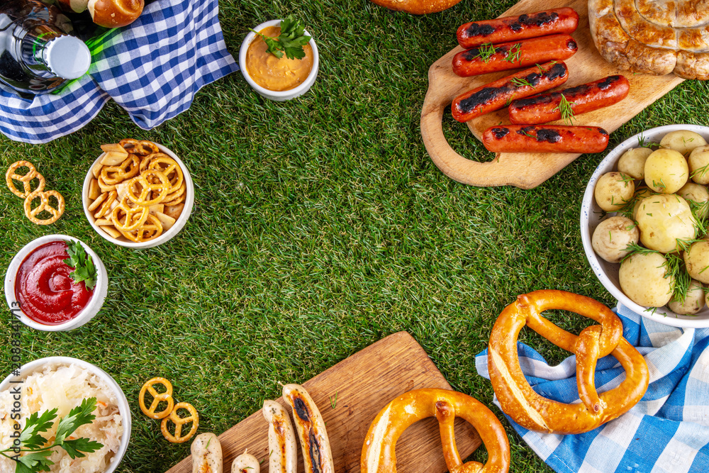Fototapeta premium Oktoberfest picnic and barbecue food, bavarian party menu, bavarian sausages, pretzels, potato, sauerkraut, beer bottles, with picnic basket, checkered napkin tablecloth, Oktoberfest festive ribbon