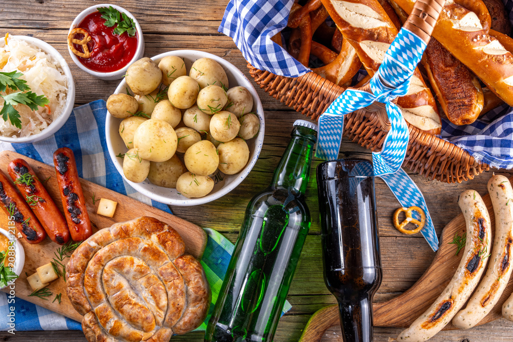 Fototapeta premium Oktoberfest picnic and barbecue food, bavarian party menu, bavarian sausages, pretzels, potato, sauerkraut, beer bottles, with picnic basket, checkered napkin tablecloth, Oktoberfest festive ribbon