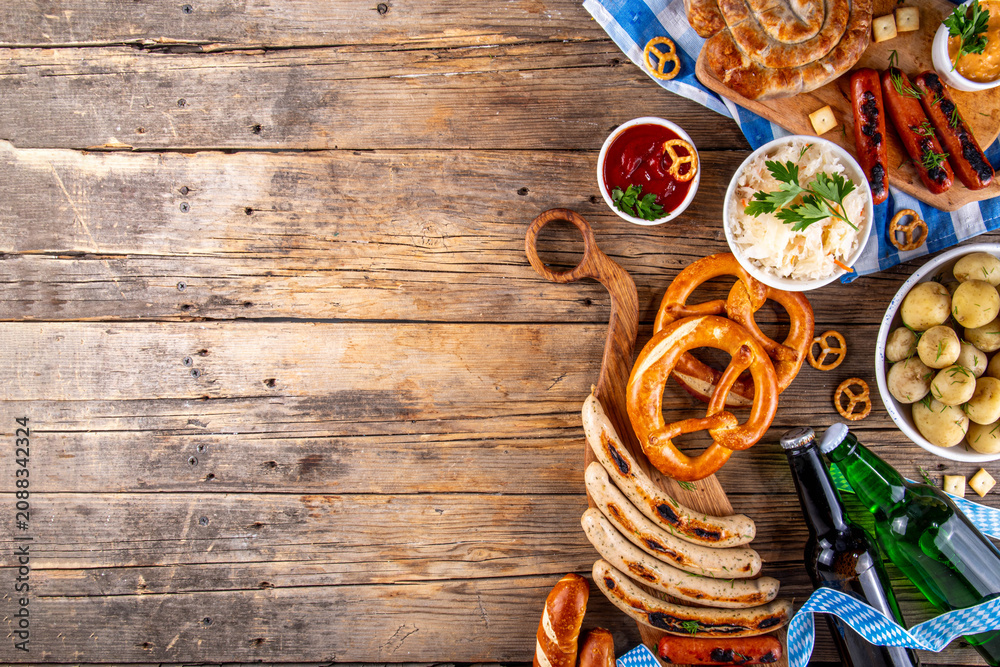 Fototapeta premium Oktoberfest picnic and barbecue food, bavarian party menu, bavarian sausages, pretzels, potato, sauerkraut, beer bottles, with picnic basket, checkered napkin tablecloth, Oktoberfest festive ribbon