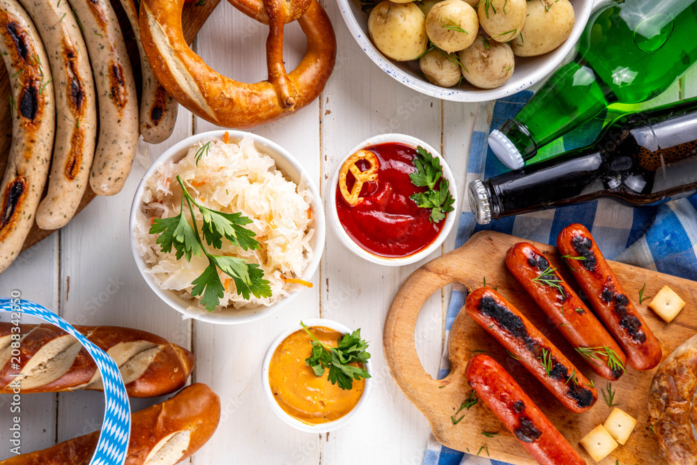 Fototapeta premium Oktoberfest picnic and barbecue food, bavarian party menu, bavarian sausages, pretzels, potato, sauerkraut, beer bottles, with picnic basket, checkered napkin tablecloth, Oktoberfest festive ribbon