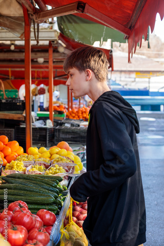 Принти на полотні A teenage boy in a black hoodie browses fresh produce at an outdoor market, exam