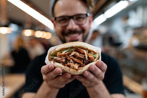Man holding grilled chicken sandwich kebab doner with lettuce and tomato in restaurant