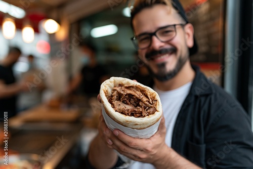 Man smiling and holding a large wrapped meat-filled burrito in restaurant, kebab doner