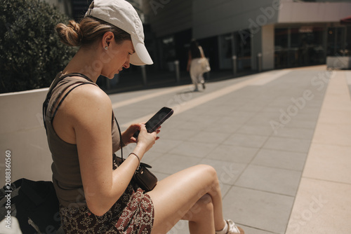 Fotografía Young woman using smartphone while resting outdoors in the city