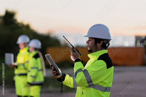 Fotografie Construction workers in high visibility gear communicating on a job site at dusk