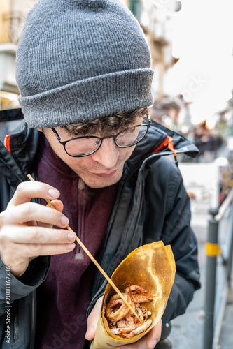 Naples, italy. December 27, 2024. Young man enjoying a delicious cuoppo of mixed fried seafood street food in spaccanapoli, naples, italy