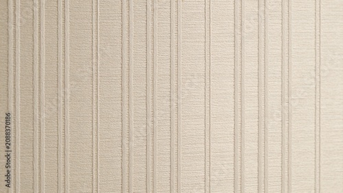 displays a close-up view of a textured surface, likely wallpaper or fabric, characterized by vertical lines and a subtle ribbed pattern. The color is a soft beige, providing a neutral and calming appe