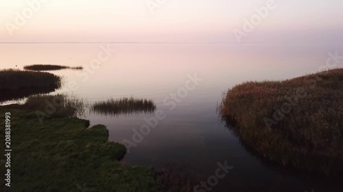 Low drone clip from the shore onto the Curonian Lagoon during sunset, in background Curonian Spit, Lithuania.
