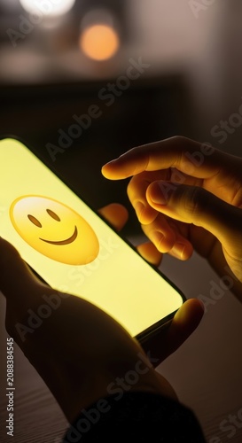 Person using smartphone with happy emoji on screen at night.