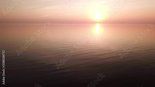 Ascending sideways drone clip above the Curonian Lagoon during sunset, in background Curonian Spit and setting sun, Lithuania.