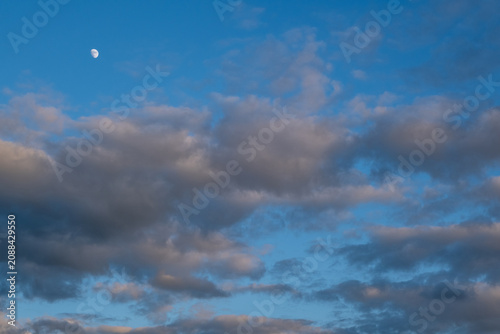 Fotografie Waxing gibbous moon in a blue sky with fluffy clouds at dusk