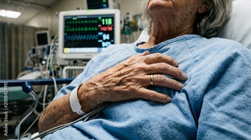 Senior patient lying in a hospital bed holding their chest with a heart monitor in the background.
