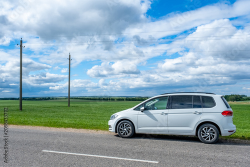 Obraz na plátně A white minivan is parked on the side of a paved road next to a green agricultur