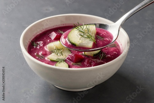 Bowl of Saltibarsciai, vibrant cold beet soup with cucumbers and dill, silver spoon resting. Concept of cold beet soup with kefir dill emphasized through colors and textures.