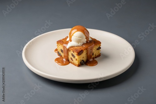 Sticky Toffee Pudding on white plate, topped with toffee sauce cream. Concept of dessert showcasing rich flavors and textures of date sponge with toffee sauce cream.