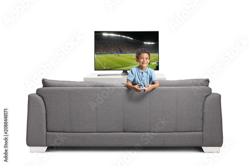 Fényképezés Little boy holding a gamepad on a sofa in front of a tv screen