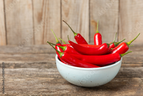 Chili pepper and chili powder on a wooden table. Red hot natural chili pepper. Organic fresh chili pepper flakes and paprika powder in a bowl on the table. Spicy spices. Copy space. Space for text.