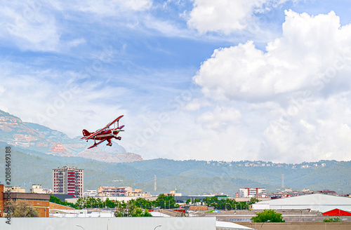 A red aerobatic biplane performing air shows in a blue sky with white clouds. Classic airplanes	