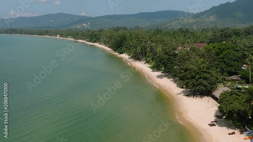 Drone view of tropical beach with turquoise water, lush vegetation, and distant mountains. Lipa Noi Beach. Ko Samui, Thailand.