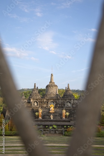 фотографія Magnificent mini replica of Borobudur temple surrounded by lush gardens, pathways, and golden Buddha statues under a blue sky at Brahma Vihara Arama monastery in Bali