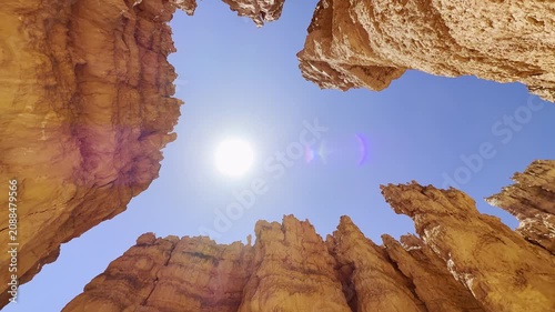 A smooth low angle cinematic shot looking up at surreal red sandstone peaks in Bryce Canyon, Utah. Majestic rock shapes under a bright sun and blue sky create an alien planet atmosphere. USA.