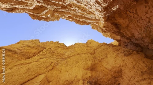 A smooth low angle cinematic shot looking up from a narrow canyon gorge at unique red sandstone spires in Bryce Canyon, Utah. Majestic otherworldly shapes against a clear blue sky. USA.