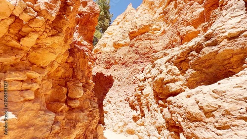 A smooth first-person POV video walking along a narrow hiking trail through a tight mountain pass in Bryce Canyon, Utah. Close-up rugged sandstone textures under a blue sky. Alien planet adventure.
