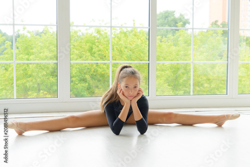 girl in sport bodysuit and ballet shoes making stretching exercise