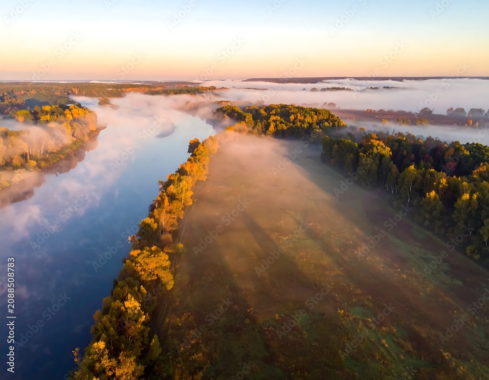 Obraz premium Misty Winding River Flowing Through Autumn Forest at Sunrise