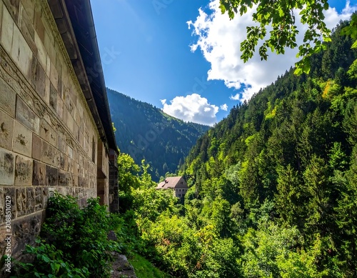 Sunlit Stone Building Overlooking Lush Forested Mountain Valley Under Blue Sky