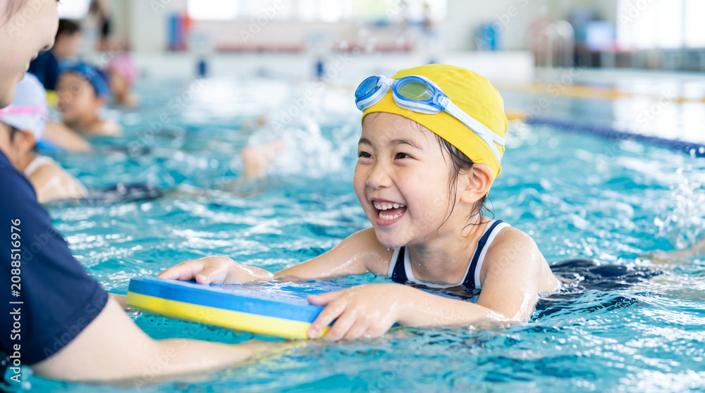 Obraz premium スイミングスクールでコーチから水泳を教わる小学生の子ども